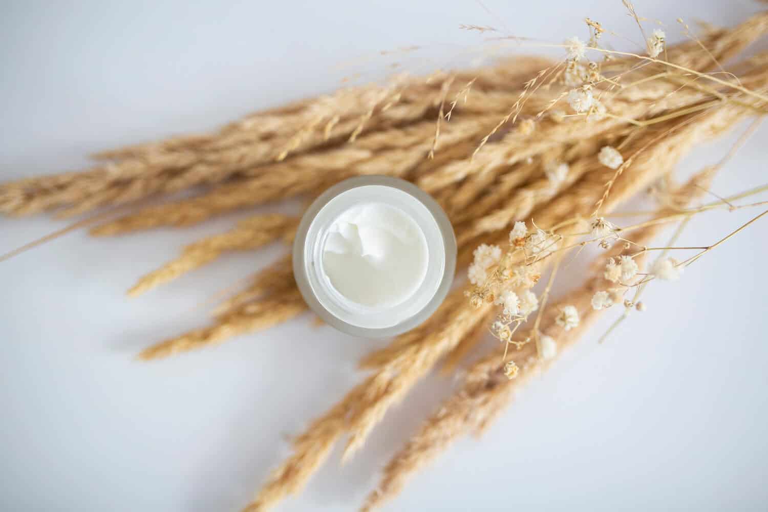 naturalny bialy krem z retinolem w sloiczku na tle wiazanki zboza