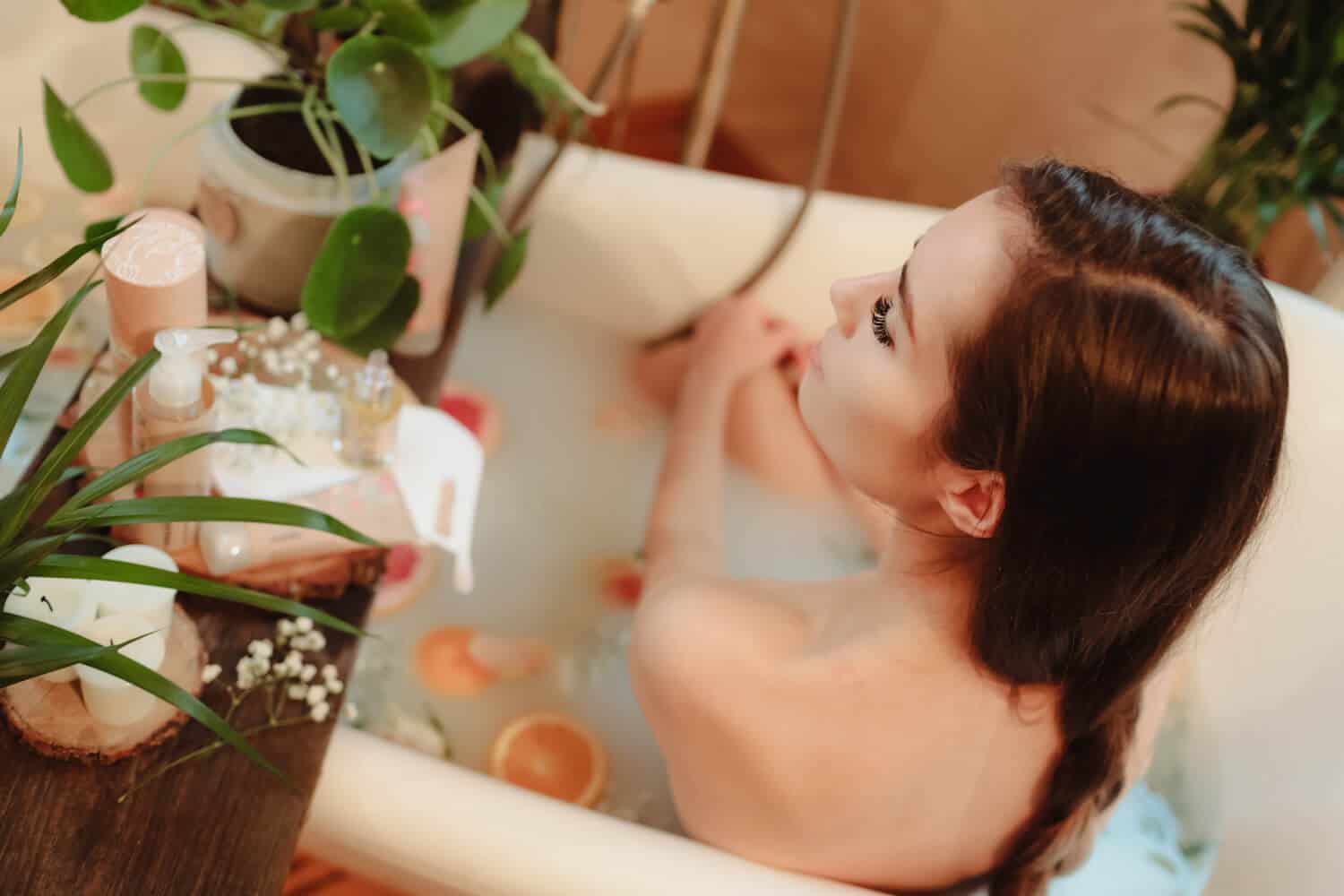 modelka brunetka wsrod kwiatow w wannie odwrócona plecami