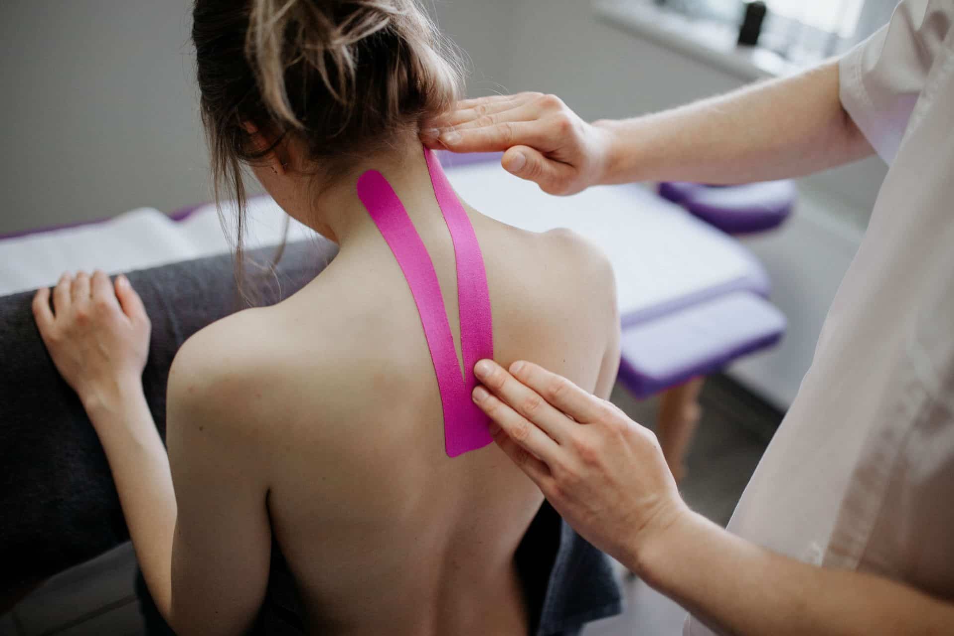 fizjoterapeuta okleja szyje pacjentki plastrami kinetycznymi